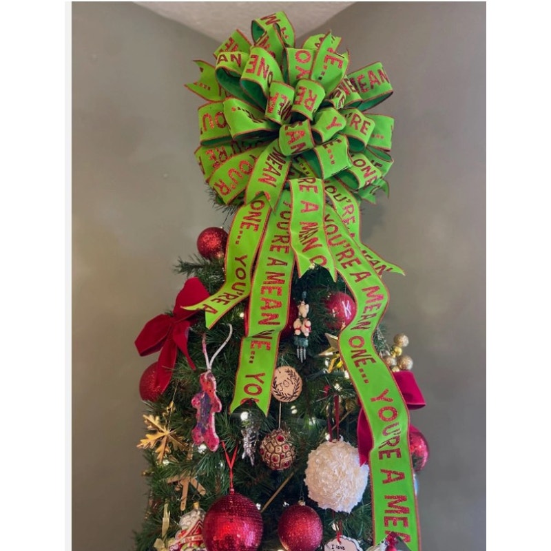 A green Christmas tree decorated with red ornaments, gold and white baubles, and a large green bow with red text that reads 'YOU'RE A MEAN V.E.